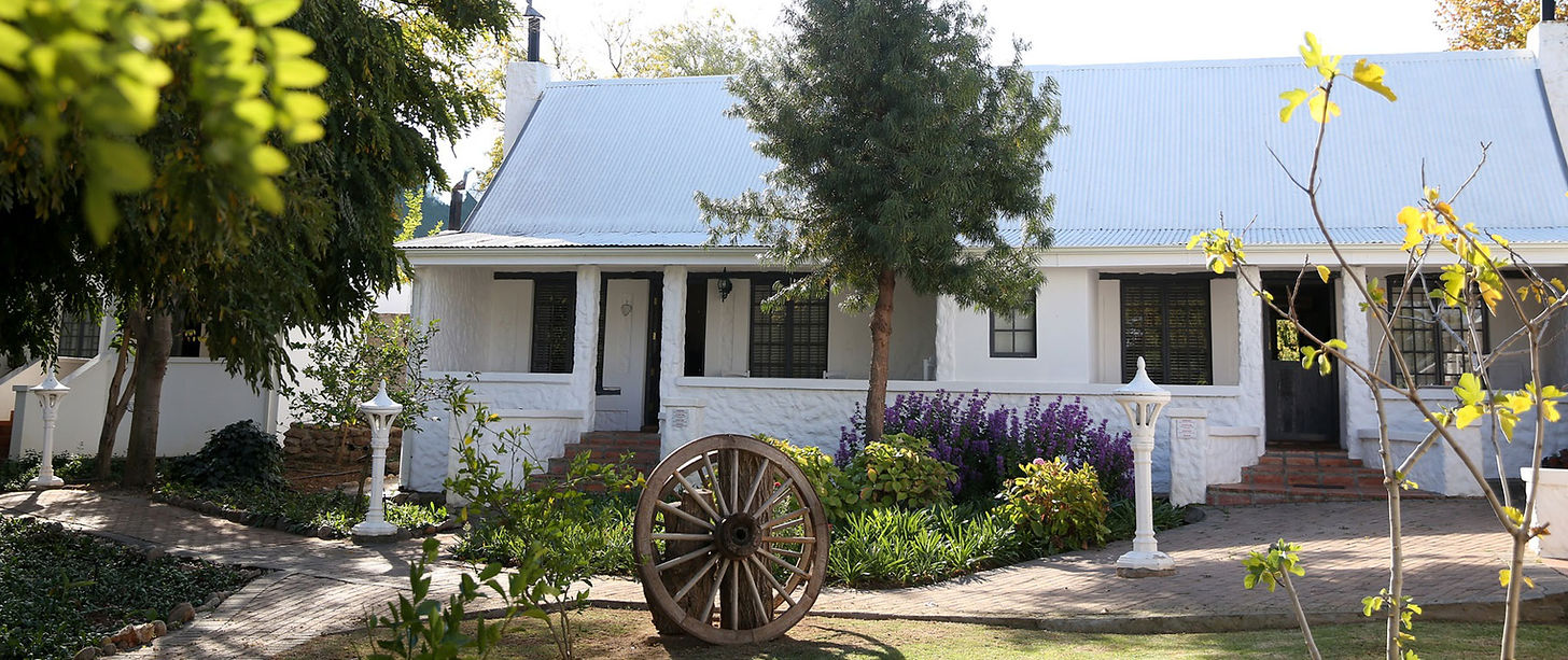 White house with blue roof, garden, and wagon wheel in front.
