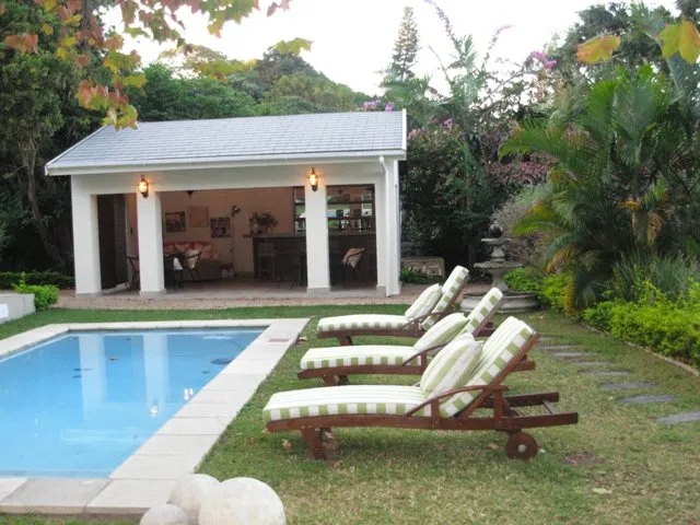 Swimming pool with lounge chairs gazebo and lush garden in the background