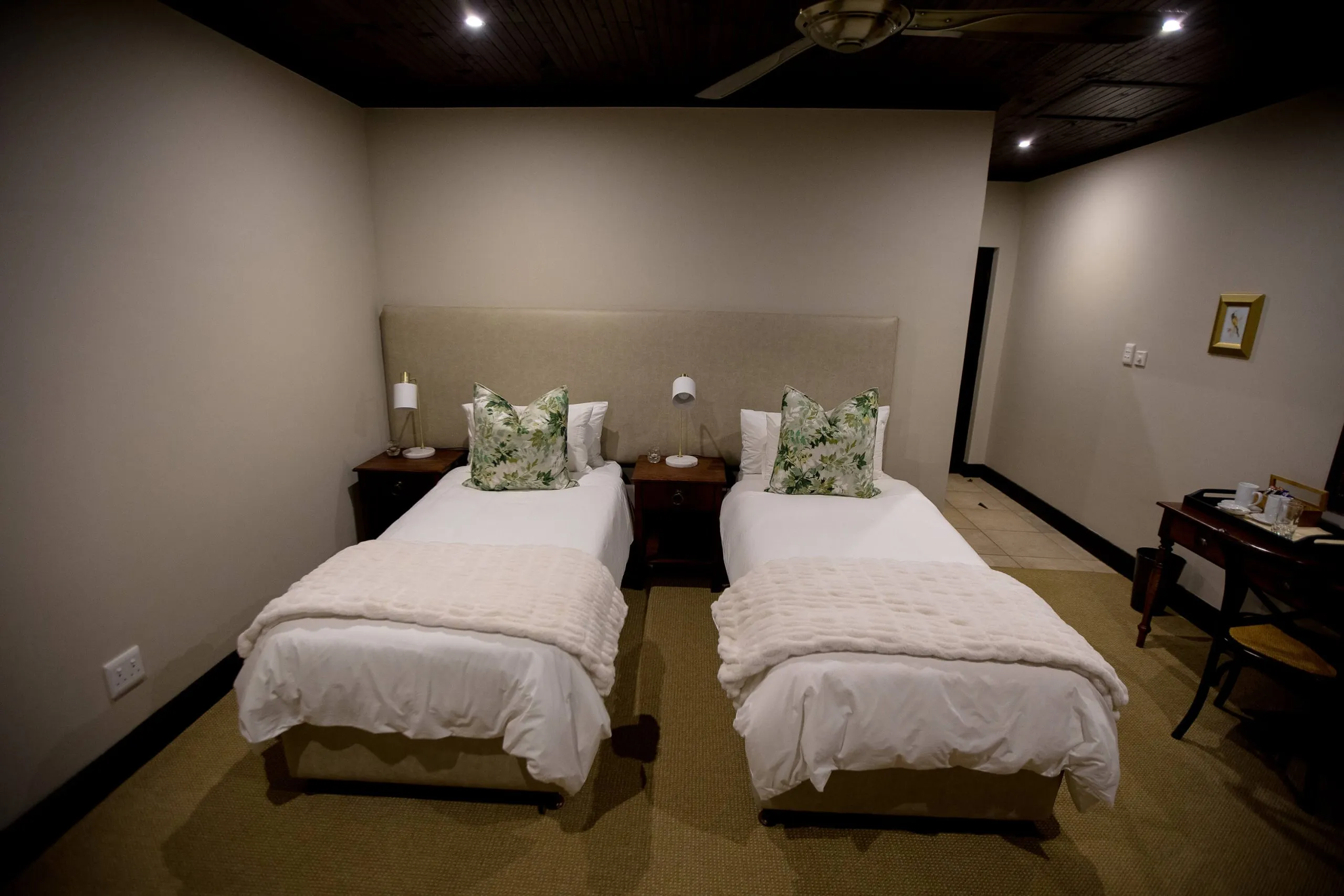 Two neatly made beds in a tidy dimly lit bedroom with wooden furniture