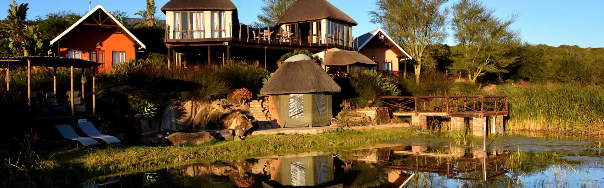 Wooden chalets by a pond with a bridge in a lush natural setting