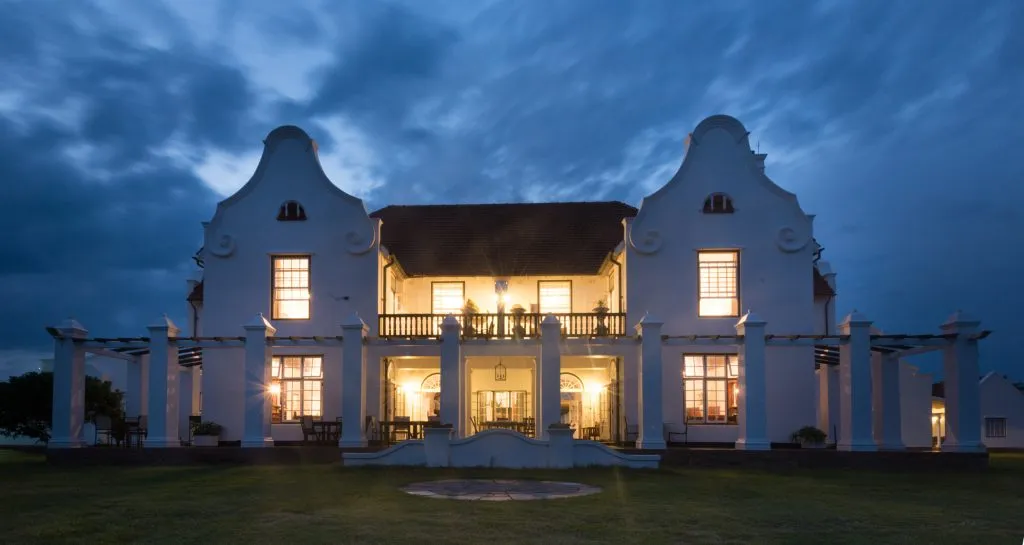 Large illuminated white house with columns and gables at night