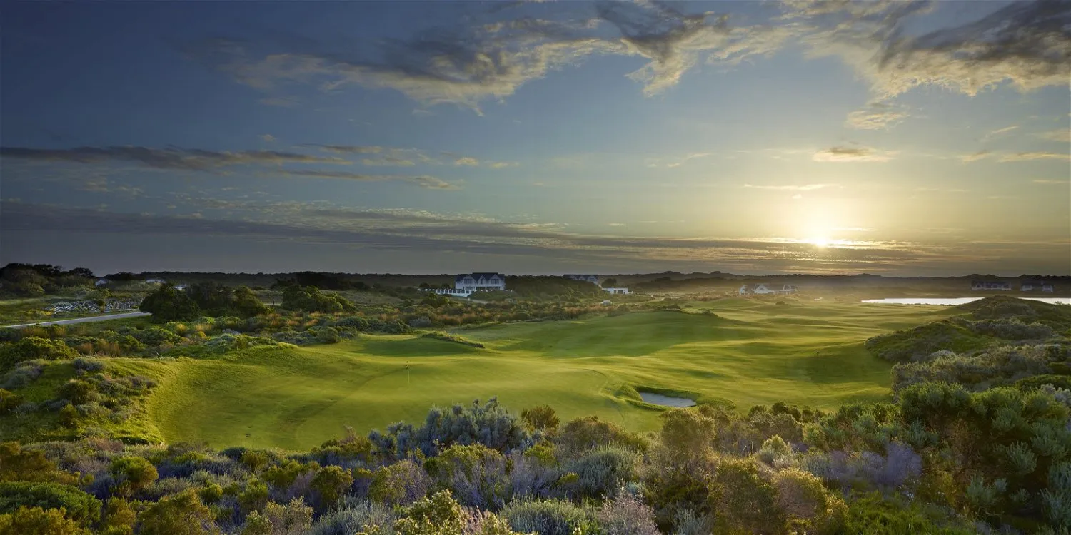 Golf course at sunset with lush greenery and distant buildings