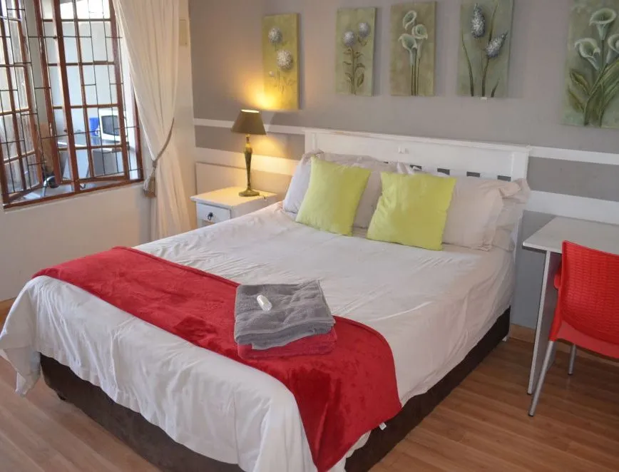 Neat bedroom with white bed red throw green pillows and wooden floor