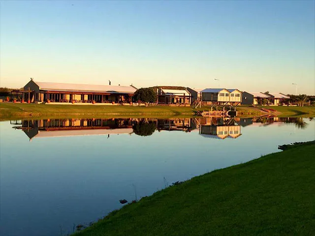 Buildings by a serene lake with green grass and a clear sky