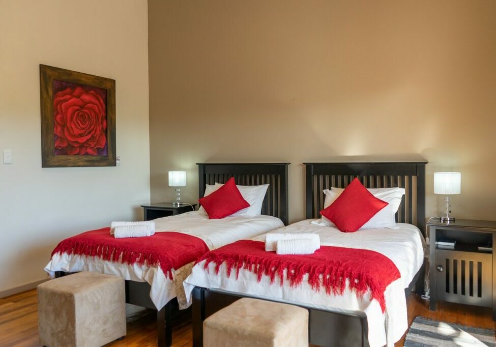 Two single beds with red blankets and pillows in a tidy bedroom.