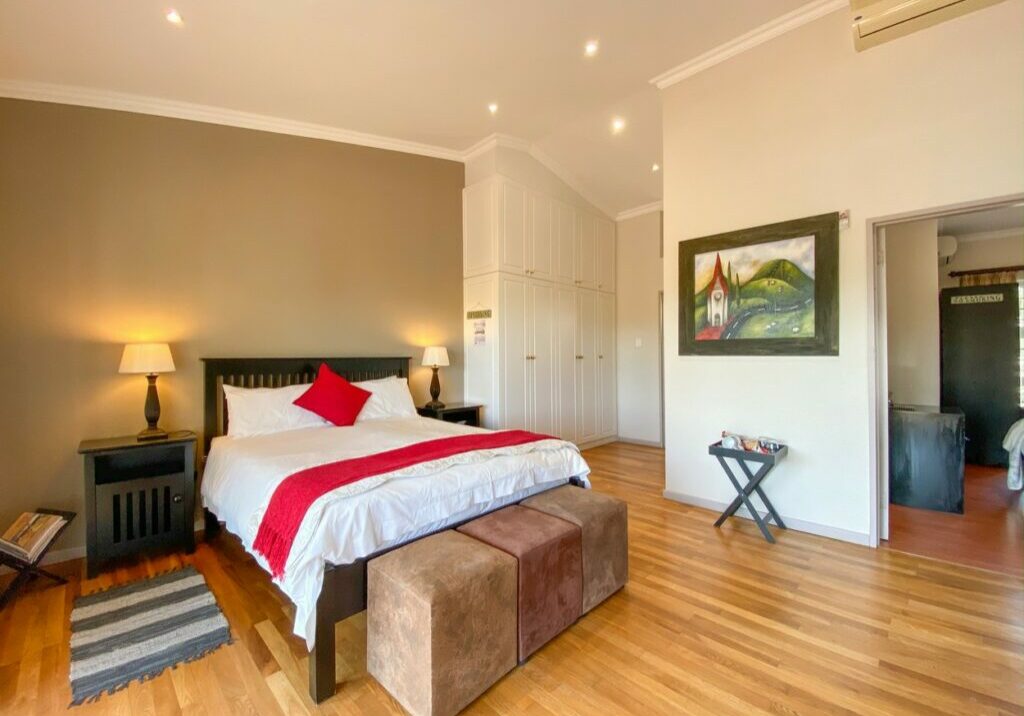 Modern bedroom with large bed, wooden floor, and artwork on the wall.
