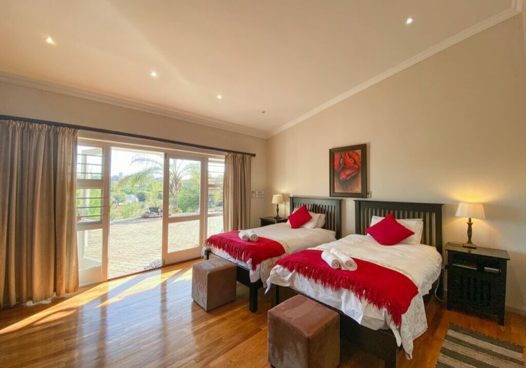 Bedroom with two beds, red decor, large windows, and wooden floor.