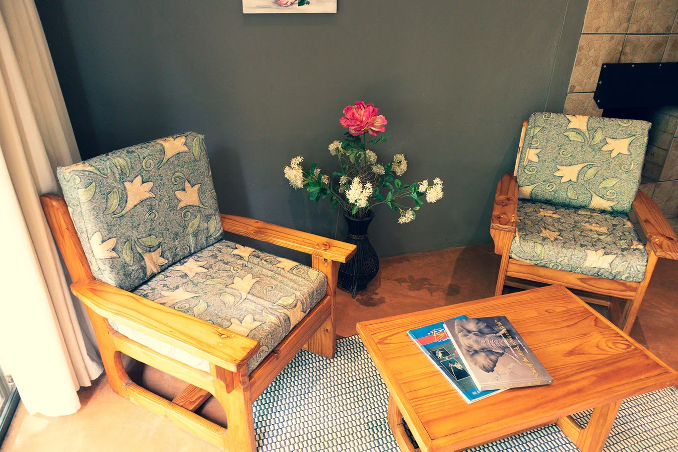 Two patterned armchairs a wooden table with magazines and a vase of flowers
