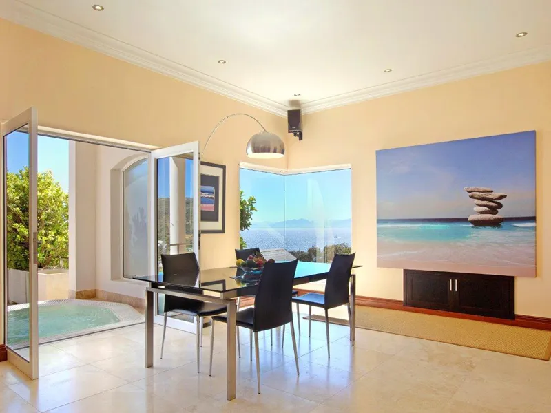 Modern dining area with glass table black chairs and ocean view painting