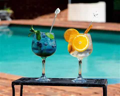 Two colorful cocktails with garnishes on a table by a swimming pool