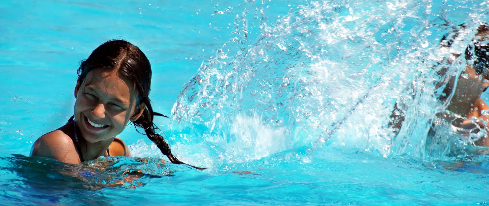 Girl smiling in a pool with water splashing around her