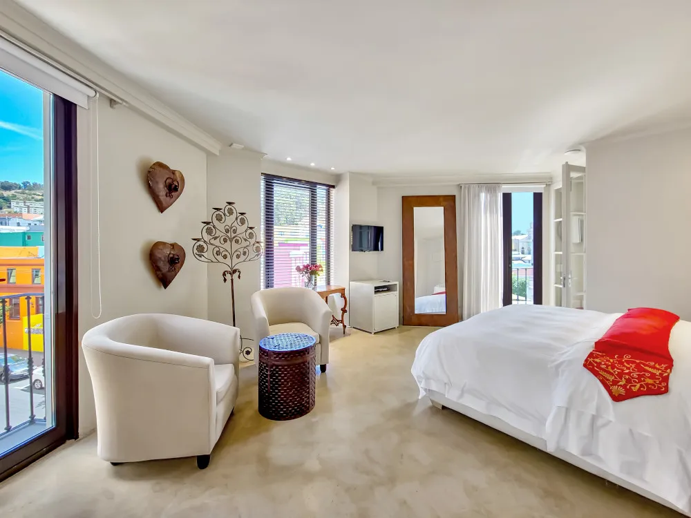 Bright bedroom with large windows white furniture and red decorative pillows