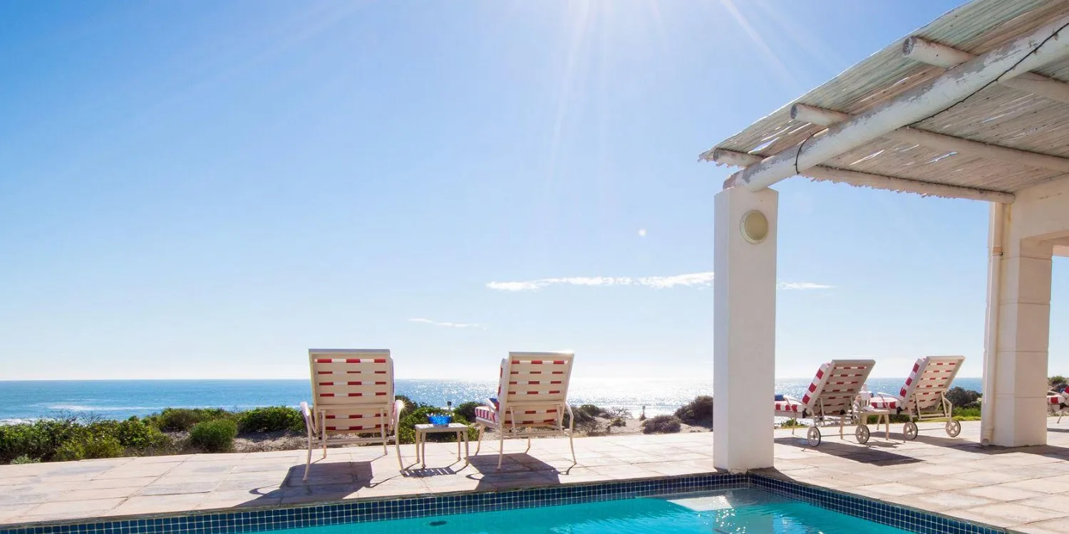 Swimming pool with lounge chairs overlooking the ocean under a sunny sky