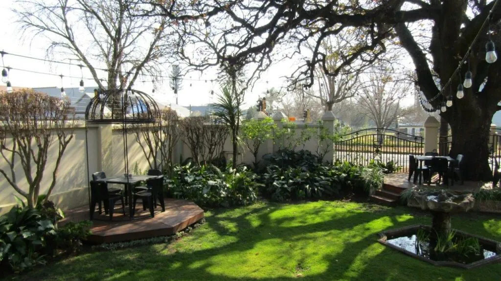 Garden with trees grass seating area and a fountain under string lights