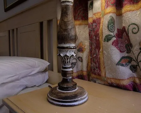 Wooden lamp on bedside table next to bed with floral curtains in background