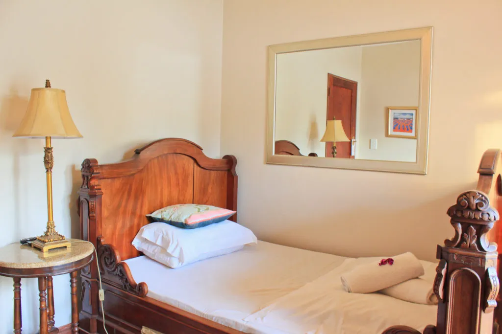 Wooden bed with white bedding bedside lamp and wall mirror in a bedroom