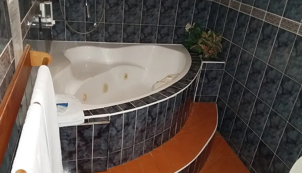 Jacuzzi tub with tiled walls wooden steps and a towel hanging nearby