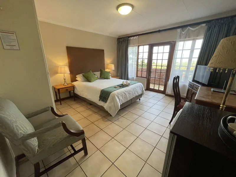 Bedroom with a bed armchair desk and large windows with curtains
