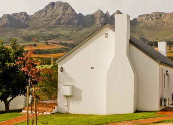 White house with chimney in front of mountains and green fields