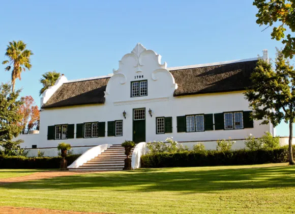 White historical building with green shutters and a thatched roof in a garden
