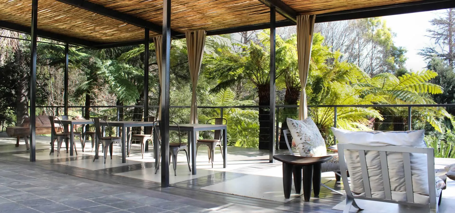 Outdoor seating area with tables chairs and lush greenery in the background