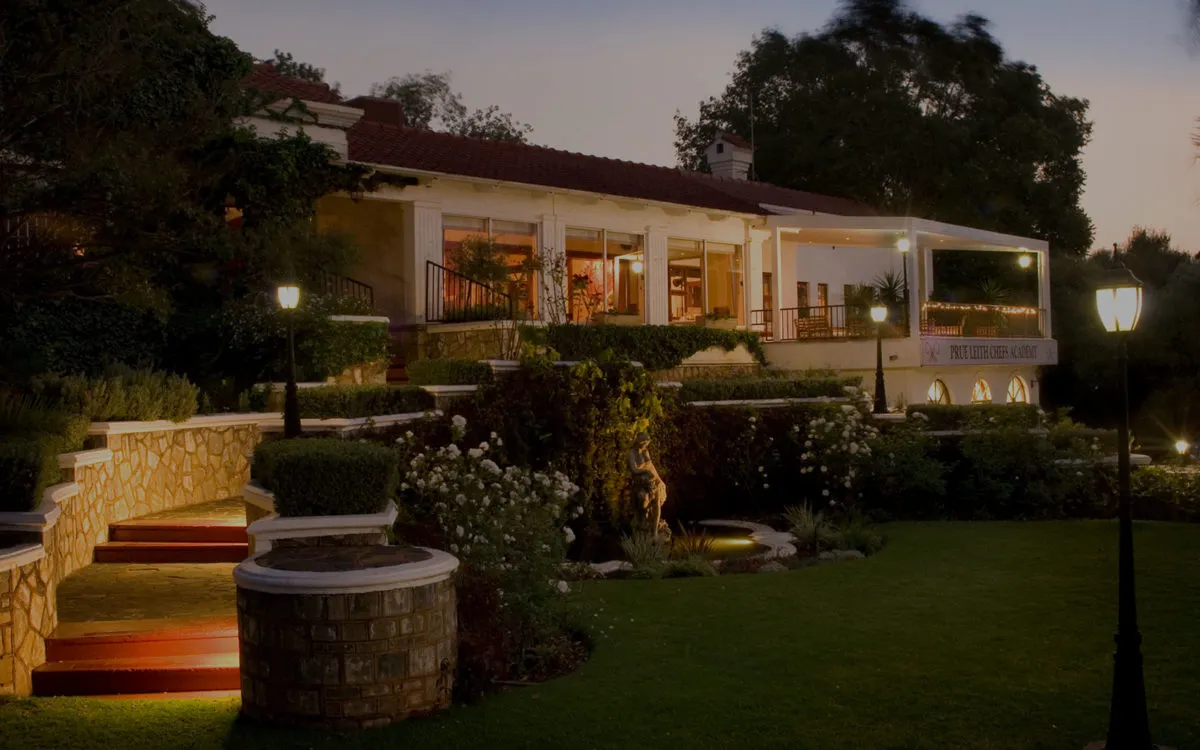 Evening view of a welllit house with lush gardens and a pathway