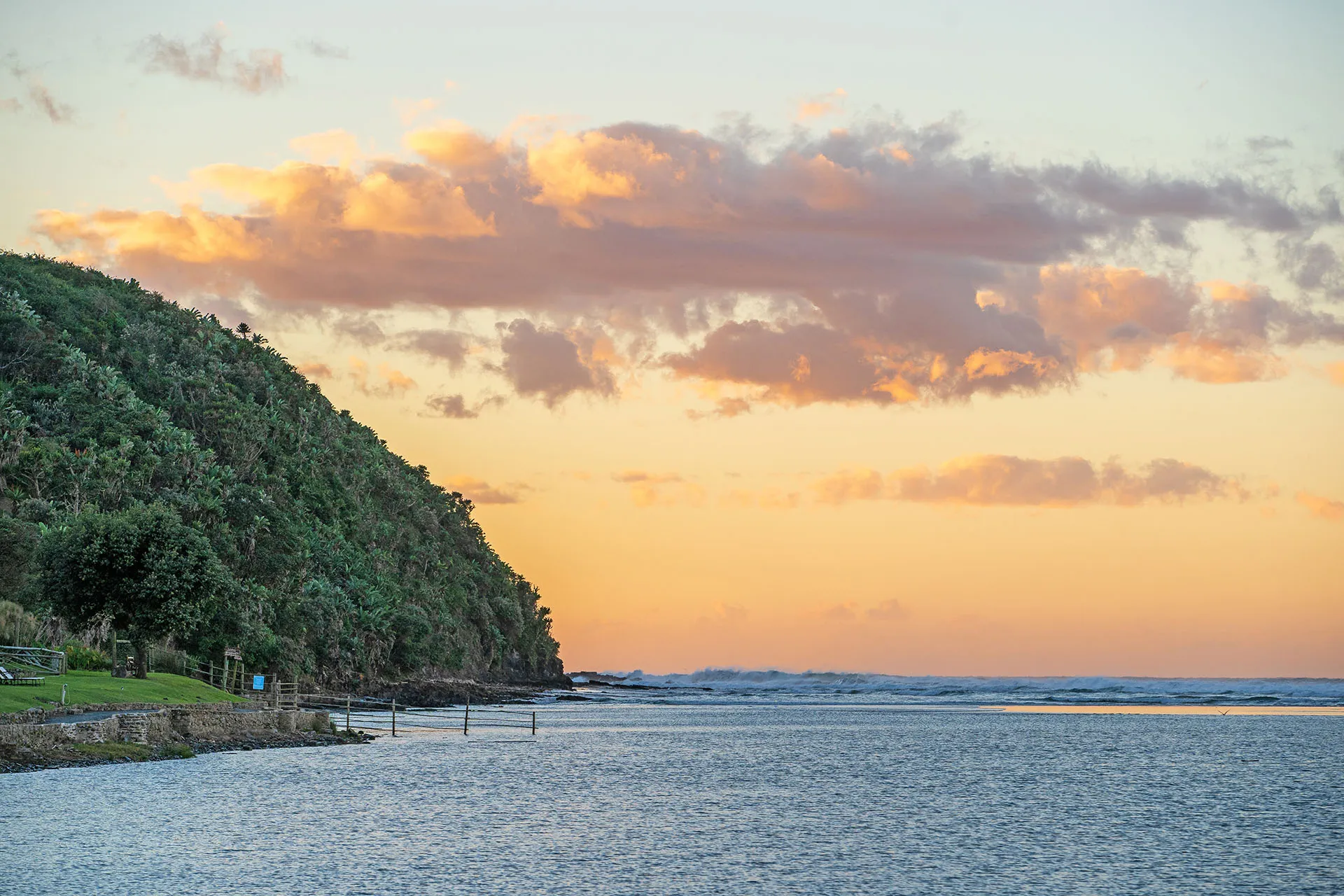 Sunset over a calm sea with a green treecovered cliff in the background