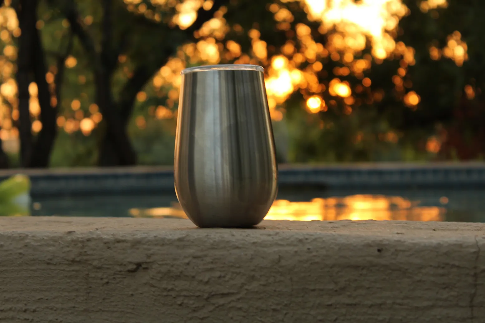 Stainless steel cup on a ledge with a sunset and pool in the background