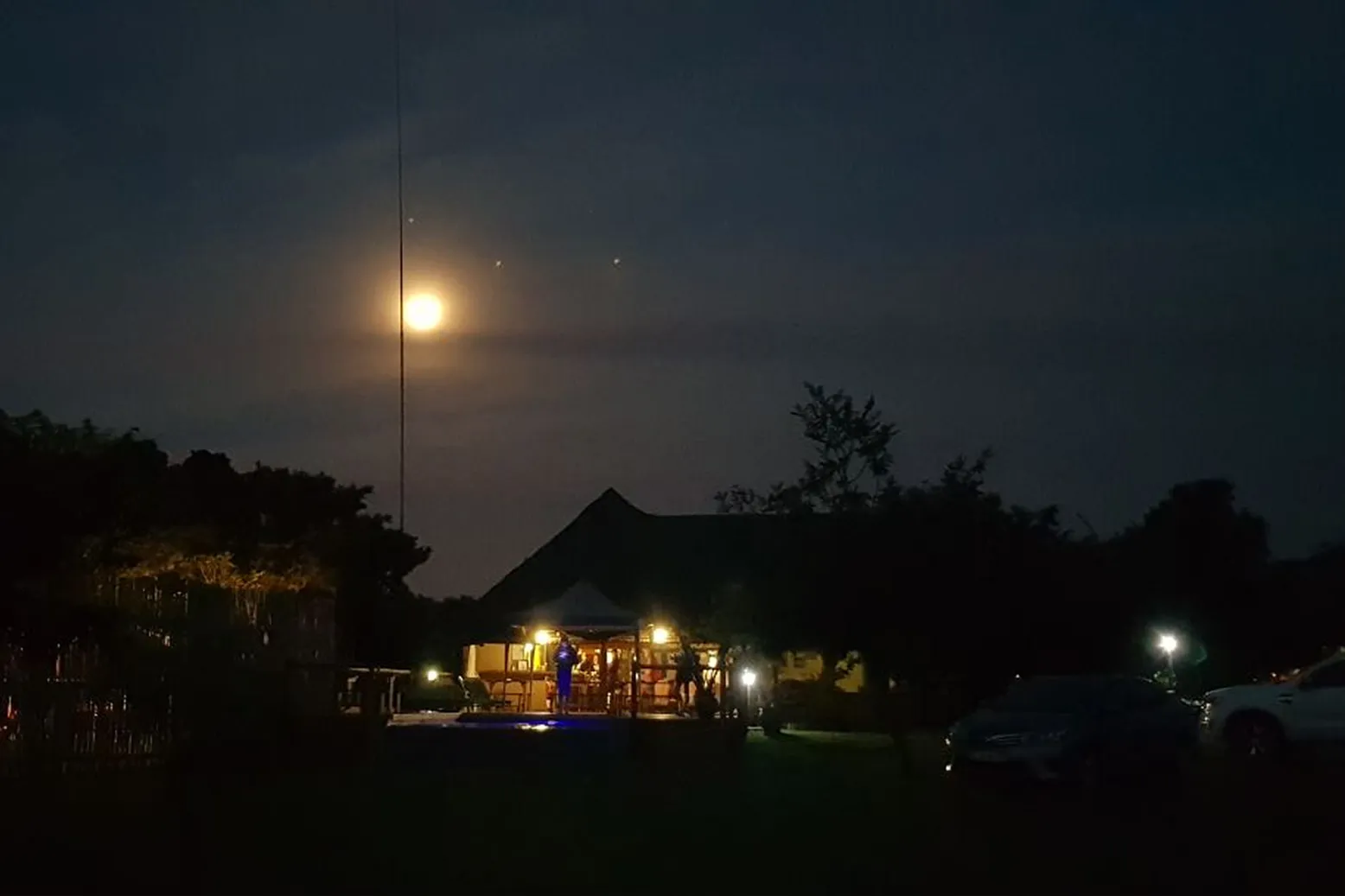 Night scene with full moon over a lit house and parked cars