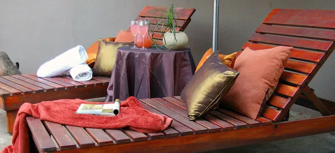 Two wooden lounge chairs with towels pillows and a table with drinks outdoors