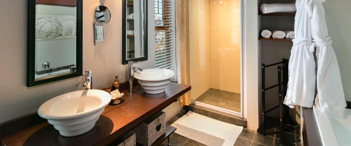 Modern bathroom with double sinks mirror shower and white robes on hooks