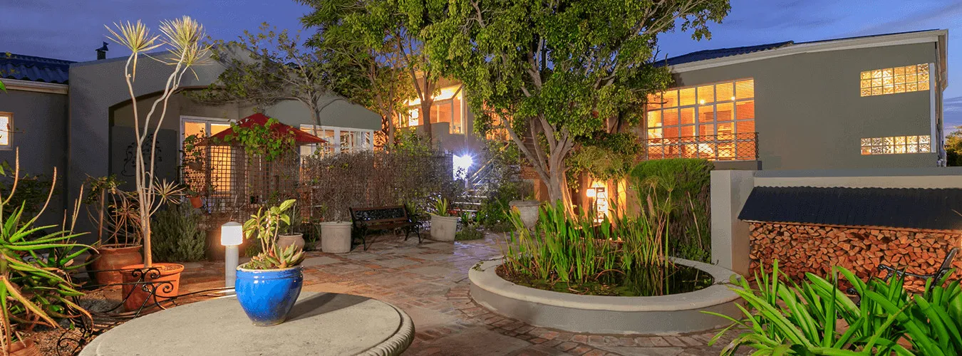 Modern house with garden potted plants and illuminated windows at dusk
