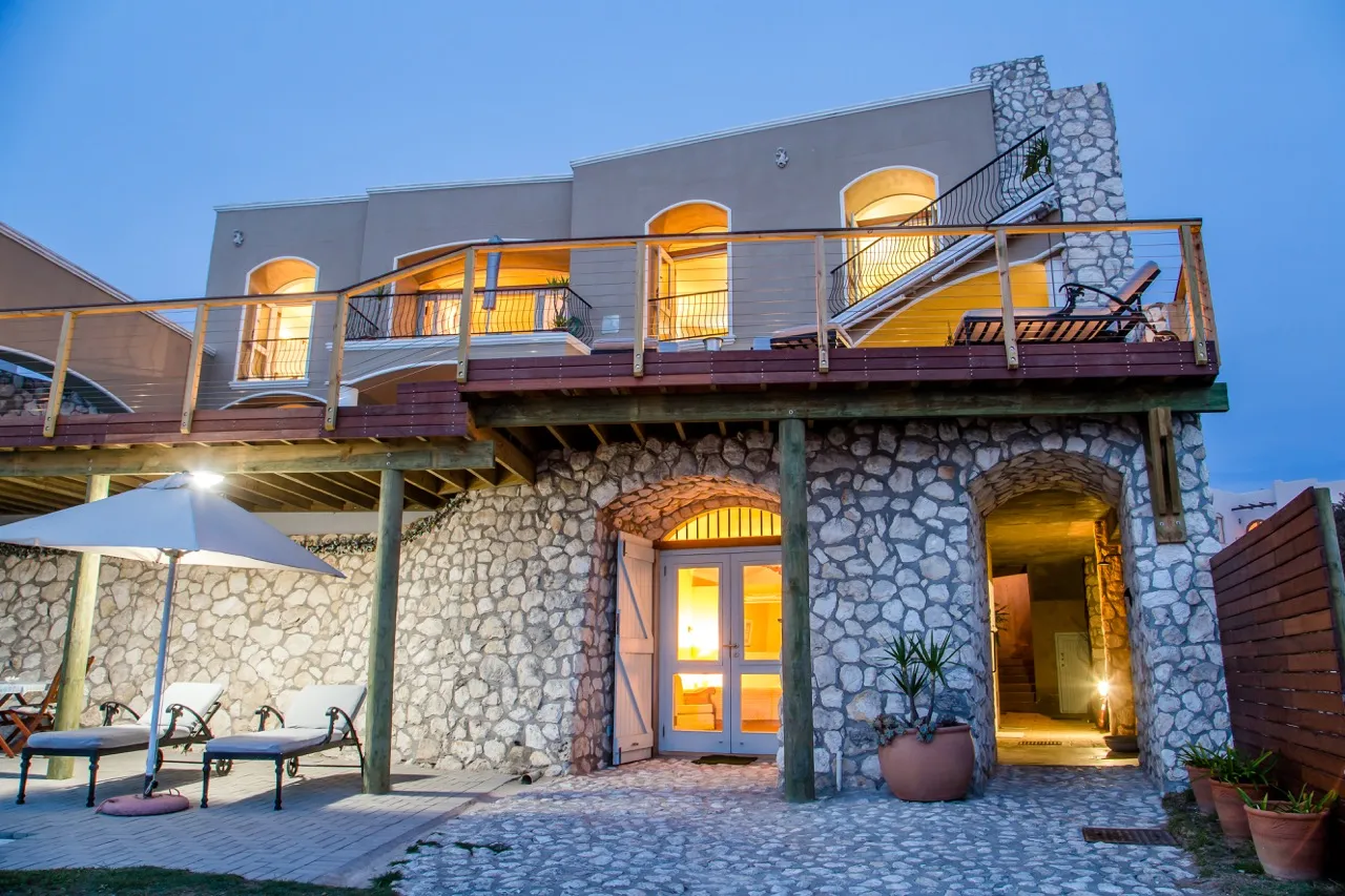 Twostory stone house with balcony and outdoor seating area at dusk