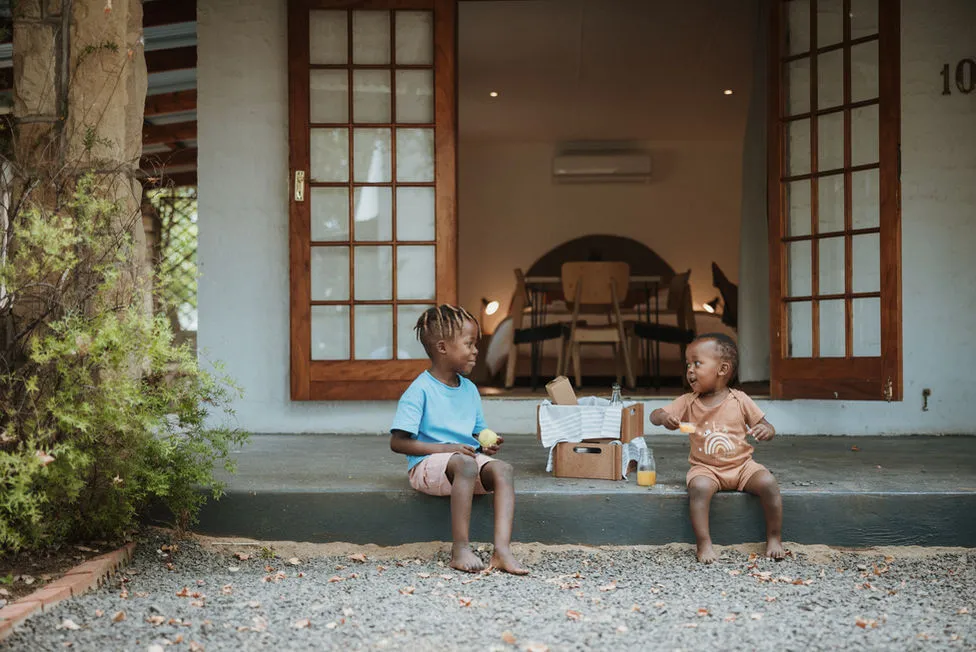 Two children sitting on steps outside a house eating and interacting