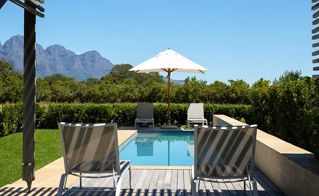 Two chairs by a small pool with an umbrella surrounded by greenery and mountains