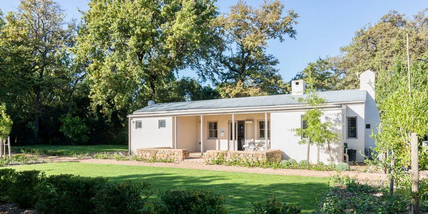 Singlestory house with a garden surrounded by trees on a sunny day
