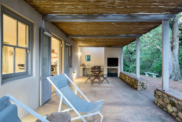 Covered patio with lounge chairs table and stone wall surrounded by greenery