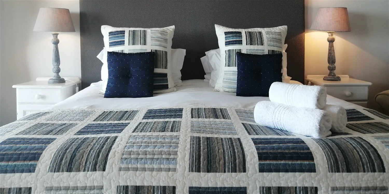 A neatly made bed with patterned pillows towels and bedside lamps