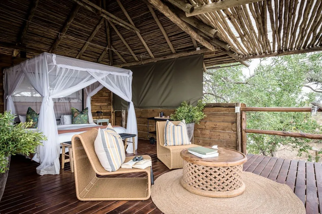 Wooden deck with wicker furniture canopy bed and tree view in a rustic setting