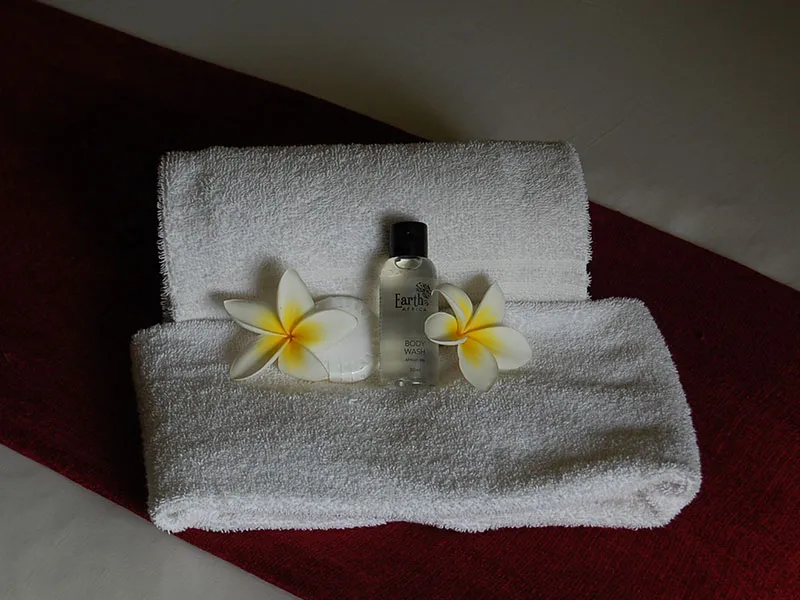 Two white towels with plumeria flowers and a small bottle on them