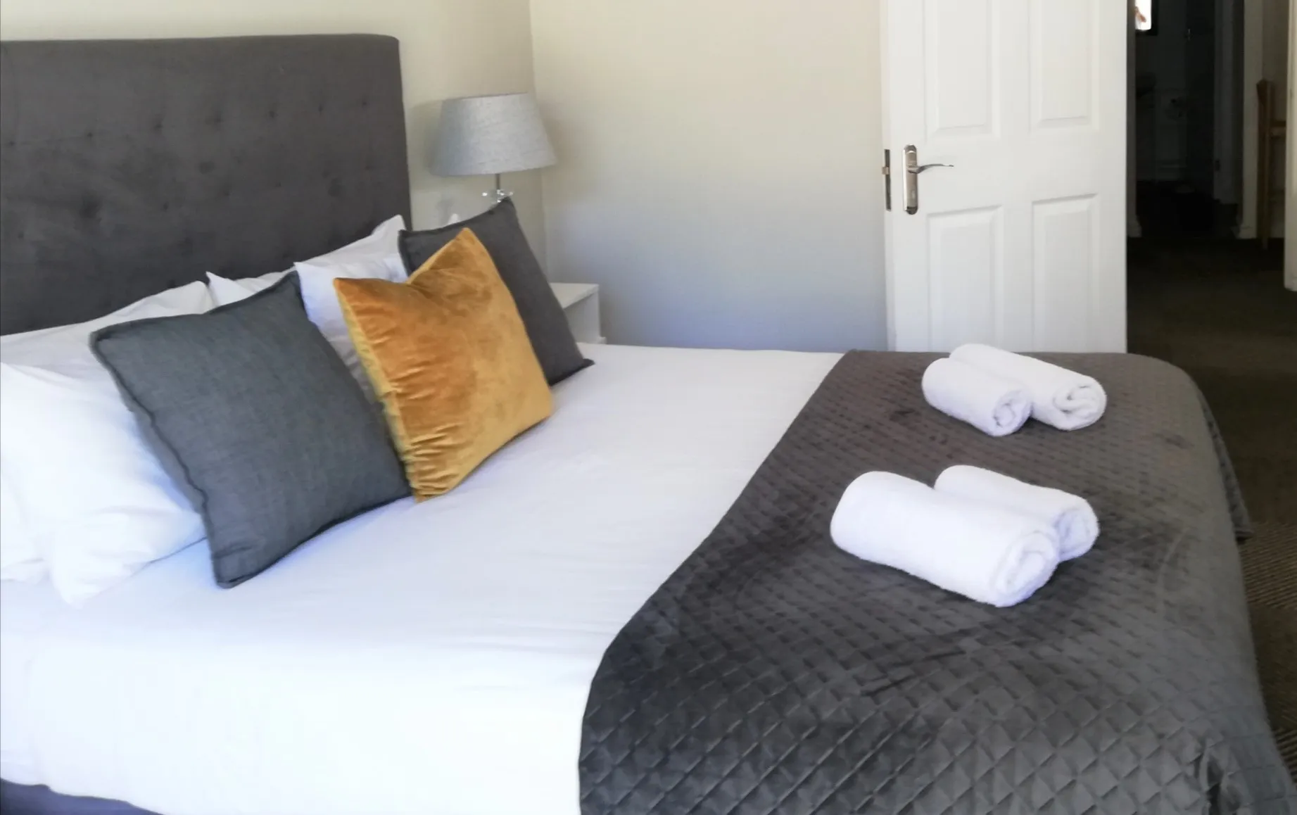 Neatly made bed with pillows towels and a bedside lamp in a bedroom